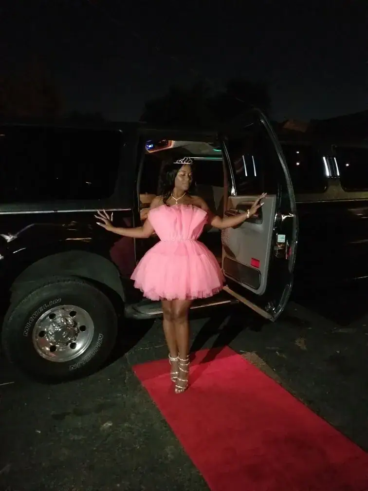Woman in a sash and crown stepping out of a white stretch SUV limousine