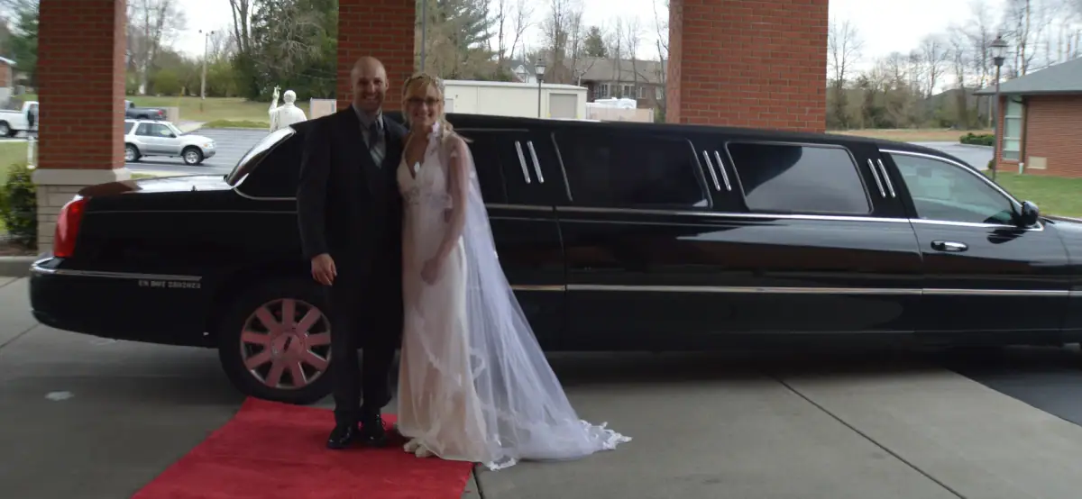 Bride and groom beside a black stretch limousine on a red carpet