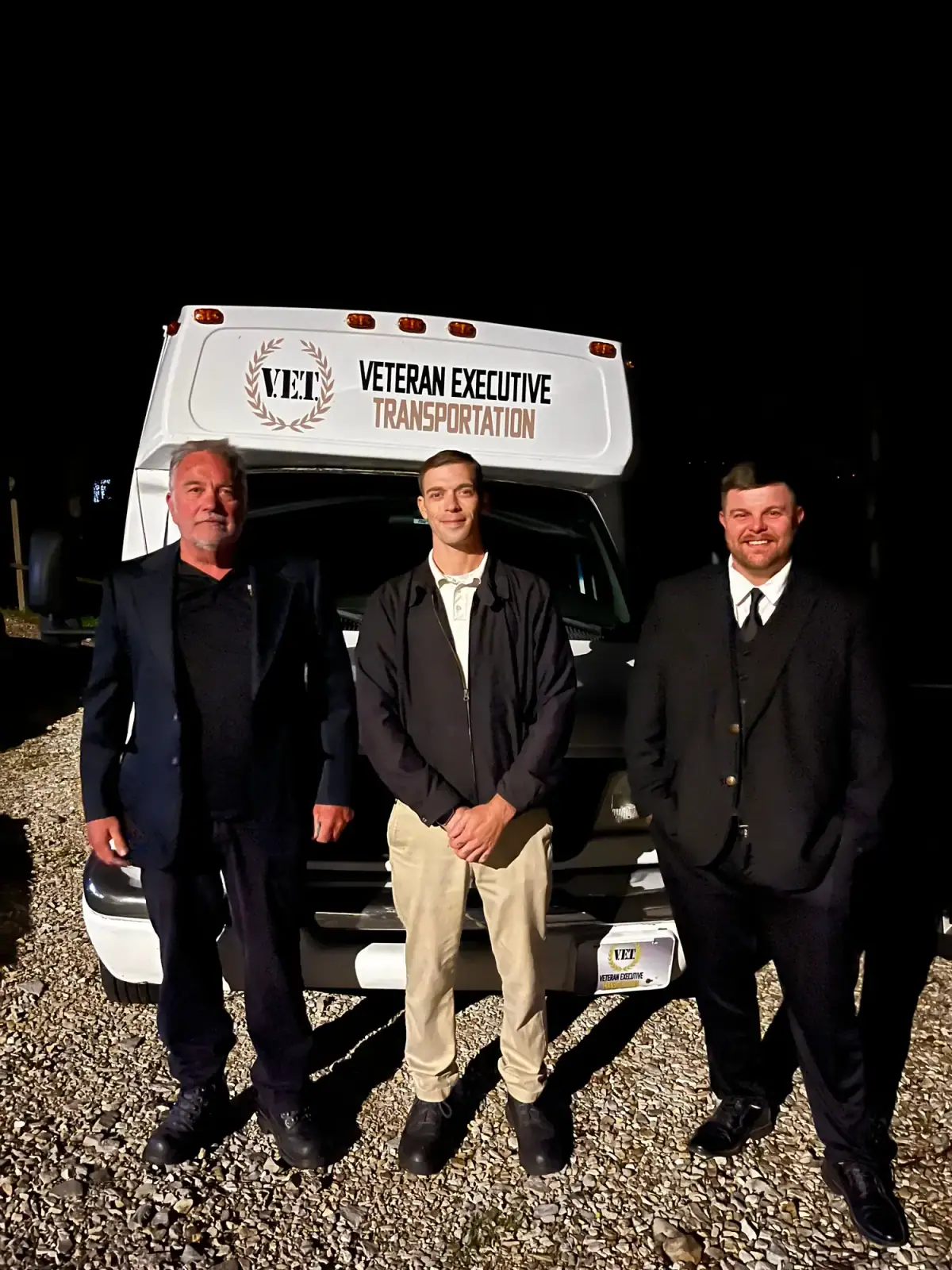 Chauffeurs standing in front of a white shuttle bus at night