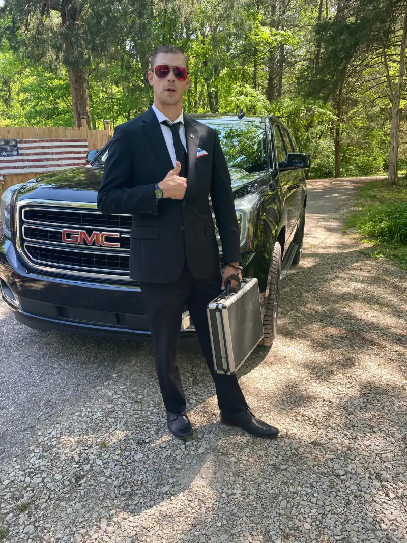 Chauffeur with a briefcase beside a black GMC Yukon