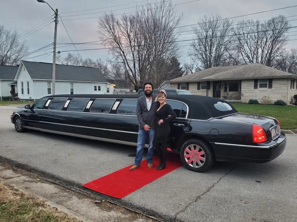 Couple on a red carpet beside a black stretch limousine