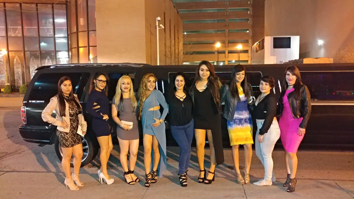 Women beside a black stretch SUV limousine at night