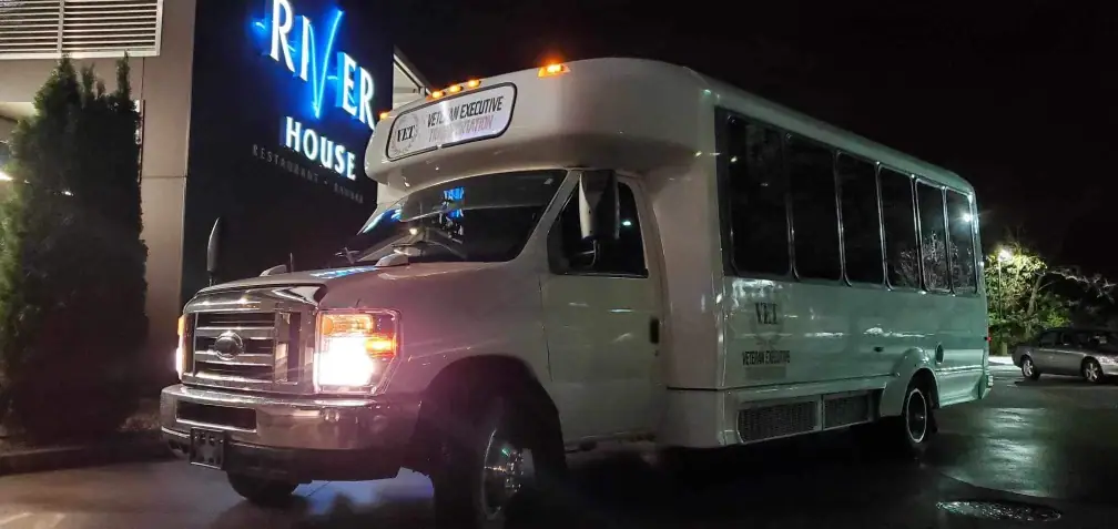 White shuttle bus lit up outside a venue at night