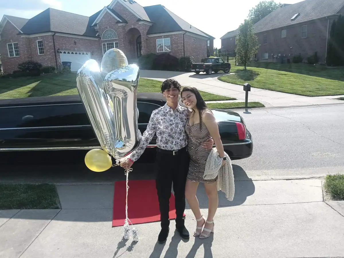 Prom couple in formal wear beside a black stretch limousine