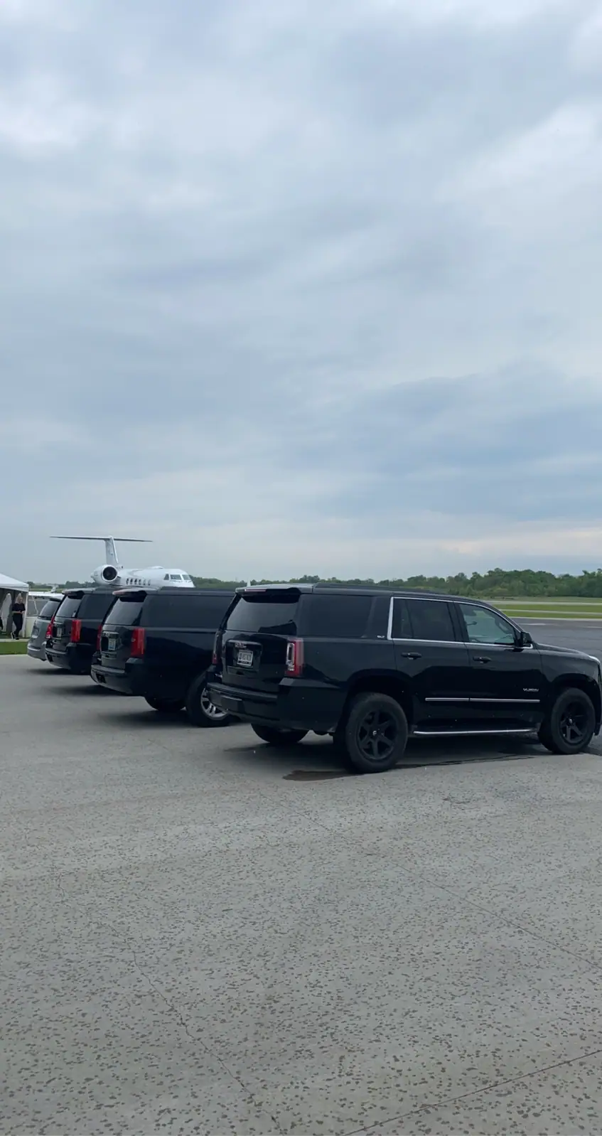 Chauffeur in a suit beside a black Cadillac Escalade and a second black SUV