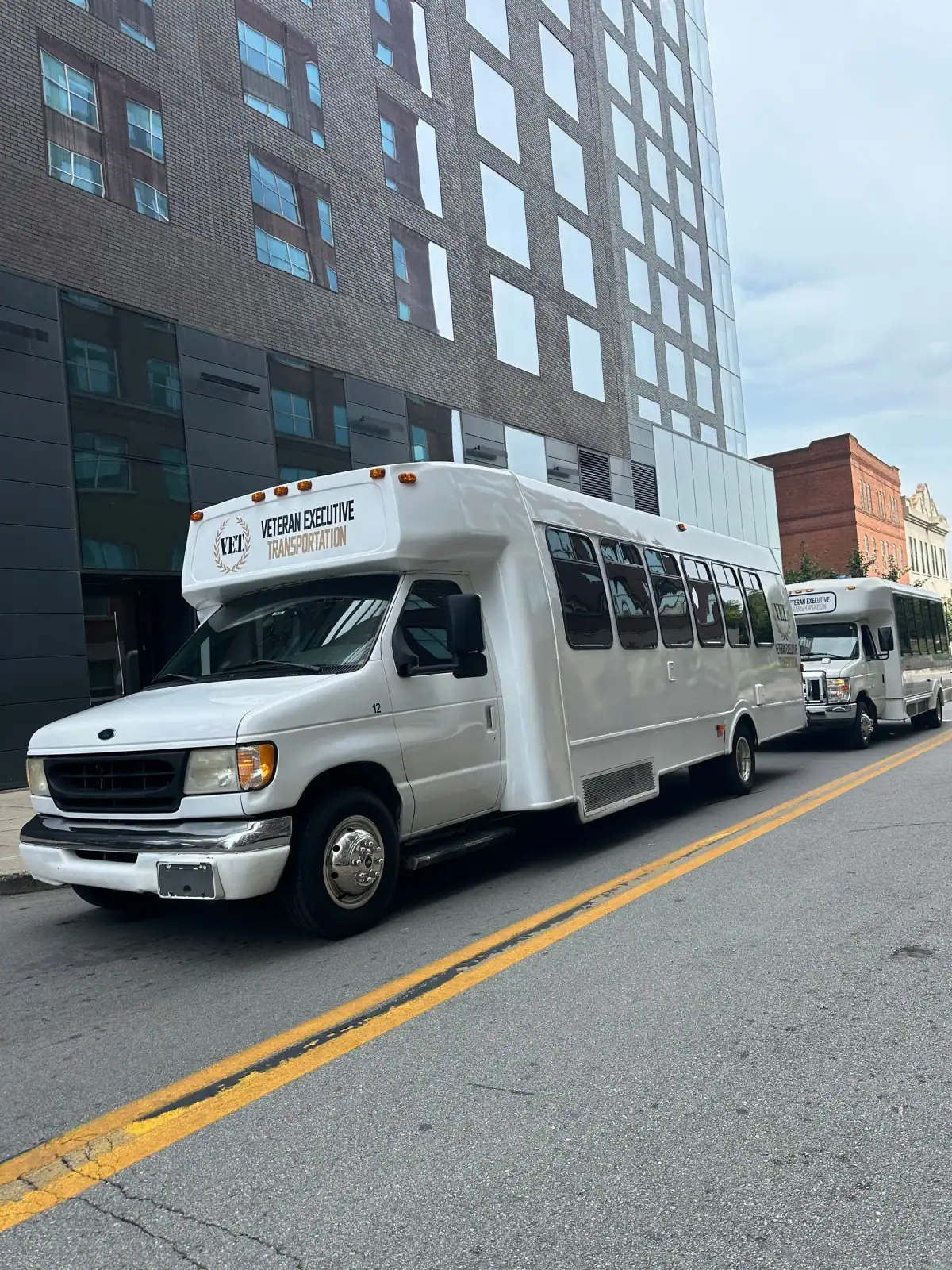 Two white shuttle buses parked on a downtown Louisville street
