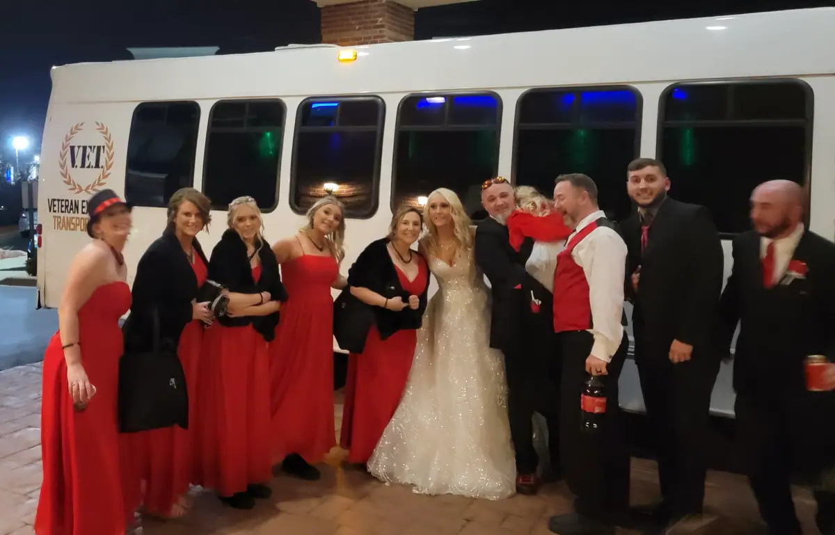 Bride and wedding party in front of the white VET party bus at night