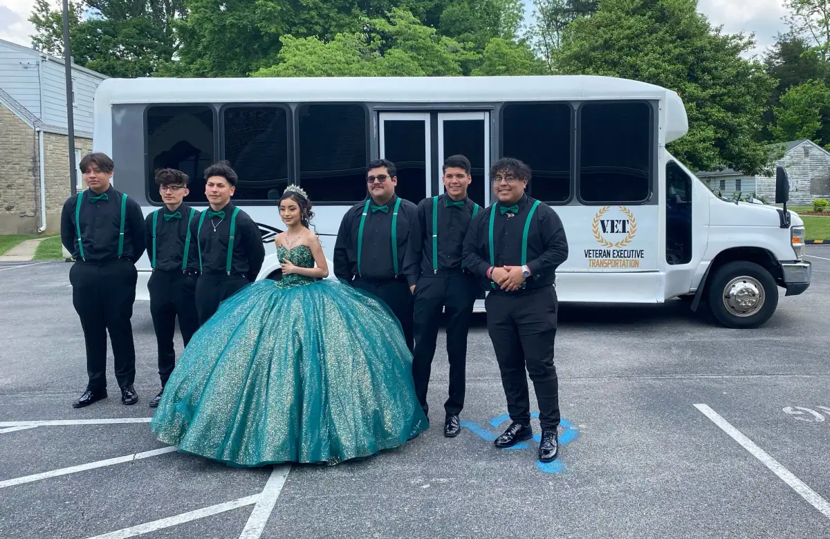 Group in formal wear in front of the long white VET party bus